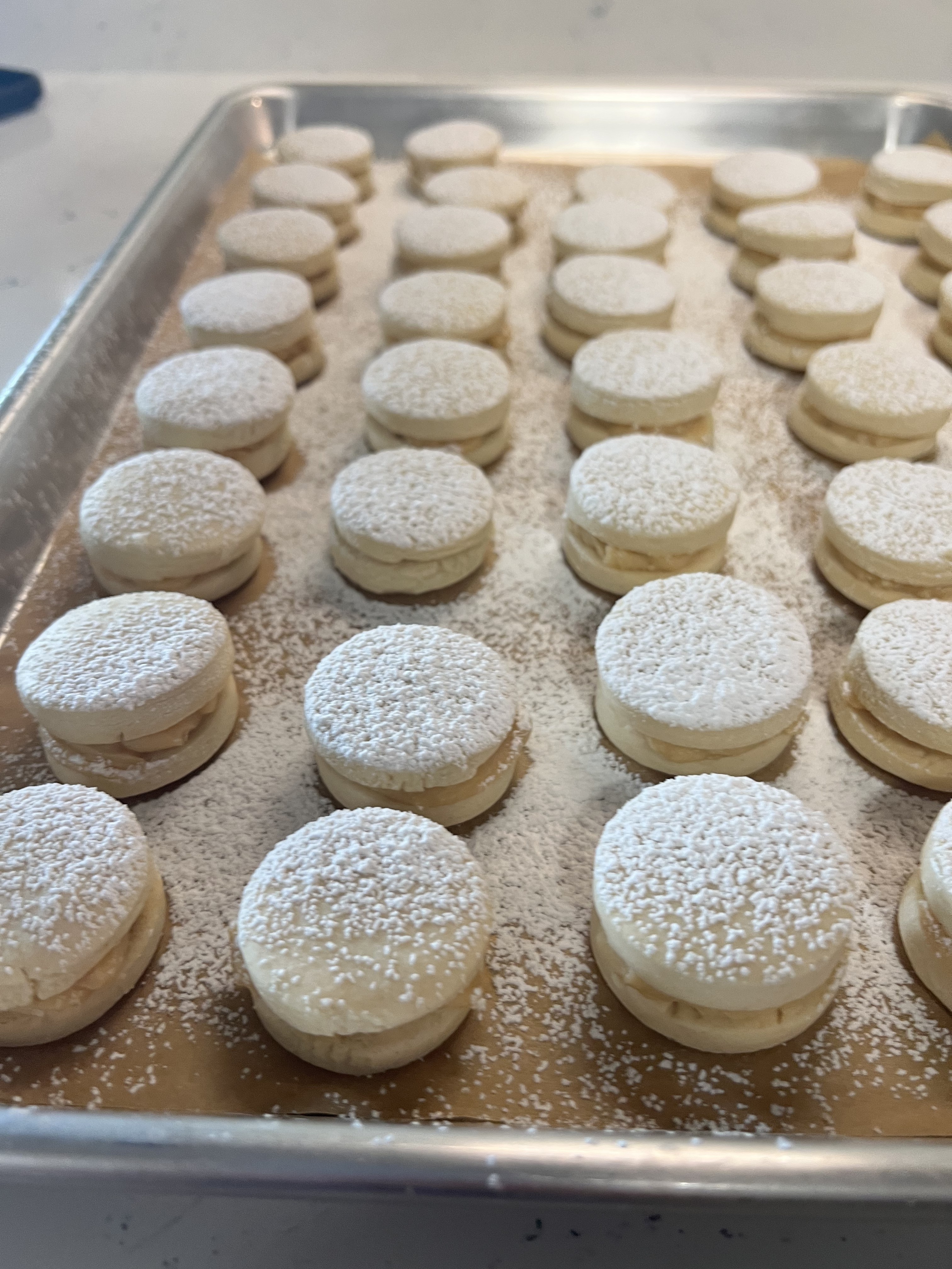 Dulce de leche alfajores dusted with powdered sugar on a baking sheet